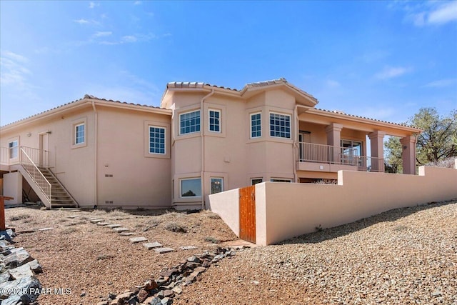 view of side of home featuring stucco siding, a tile roof, stairs, and fence