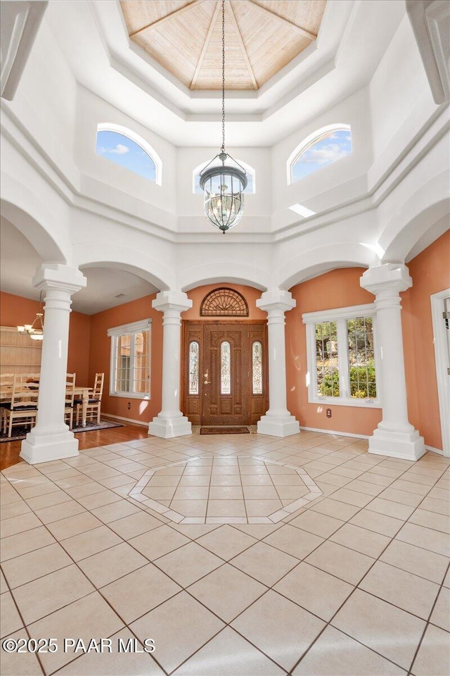 foyer featuring baseboards, a chandelier, a tray ceiling, arched walkways, and light tile patterned flooring