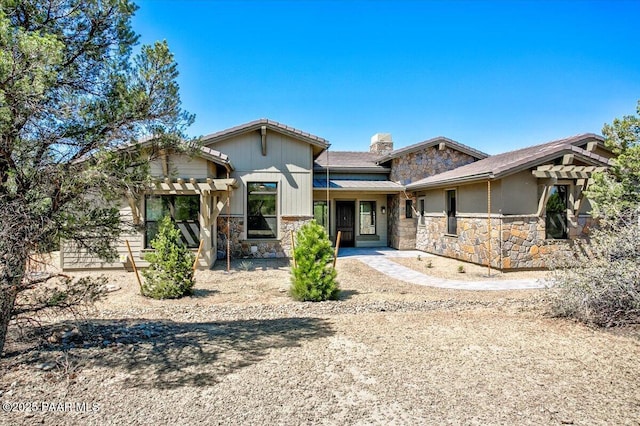 view of front of property featuring stone siding, a pergola, and a chimney