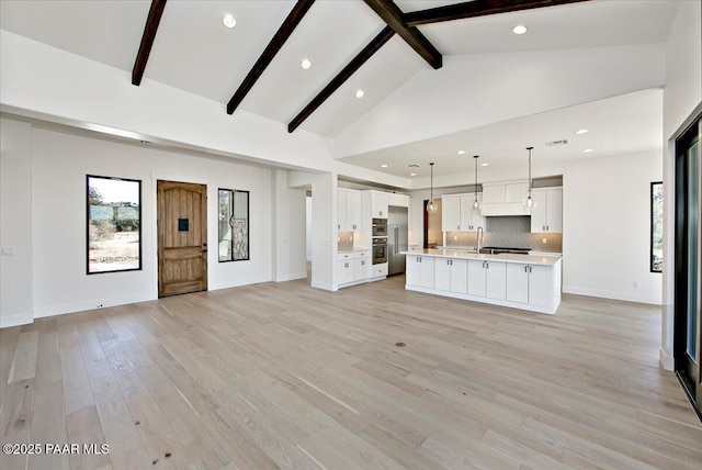 unfurnished living room featuring a sink, light wood-type flooring, vaulted ceiling with beams, baseboards, and recessed lighting
