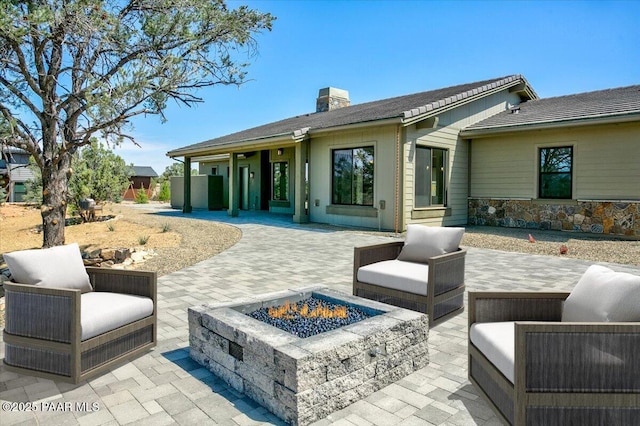 back of property with stone siding, a chimney, a patio, and an outdoor fire pit
