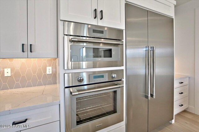 kitchen with light stone counters, stainless steel appliances, backsplash, light wood-style flooring, and white cabinetry