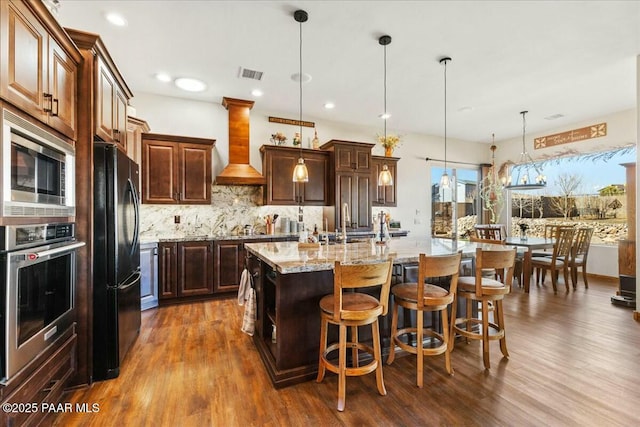 kitchen with visible vents, decorative backsplash, custom range hood, appliances with stainless steel finishes, and a kitchen bar