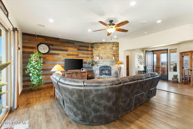 living area featuring a ceiling fan, wood finished floors, recessed lighting, wooden walls, and a fireplace