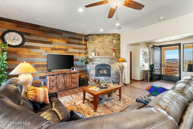 living room featuring a ceiling fan, wood finished floors, visible vents, and a fireplace