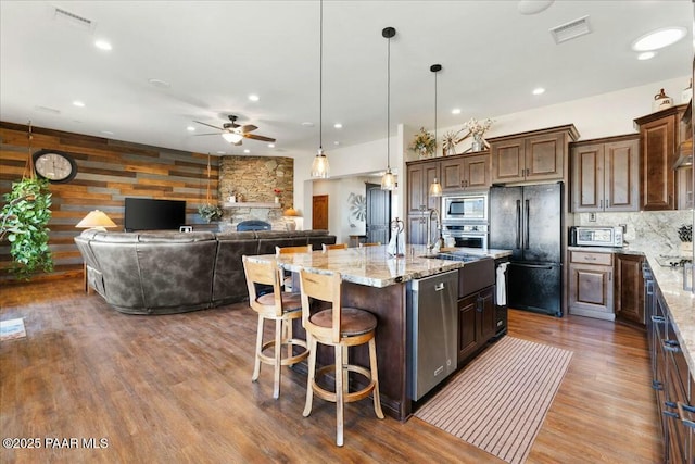kitchen featuring visible vents, light stone counters, dark wood-style floors, stainless steel appliances, and a ceiling fan
