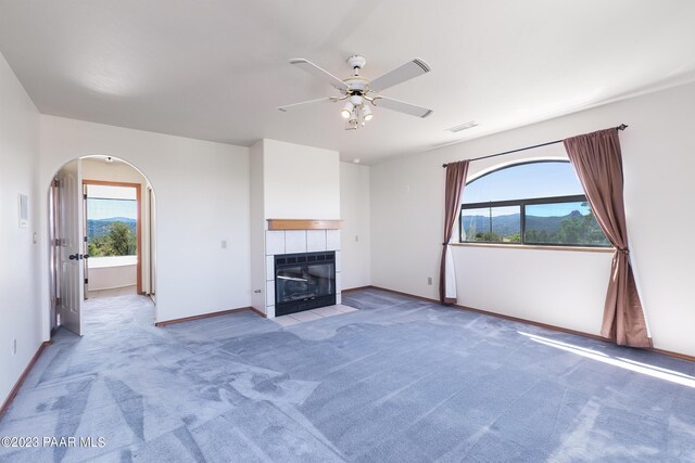 unfurnished living room featuring a tile fireplace, a wealth of natural light, ceiling fan, and light colored carpet