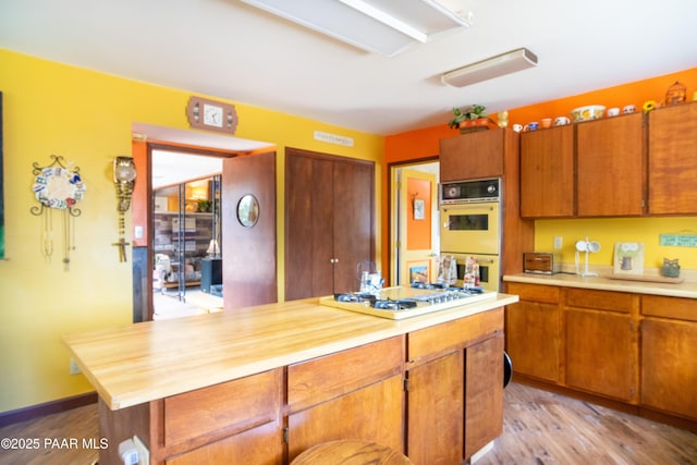 55409 Madre Cir, Seligman, AZ 86337 - kitchen with double oven, white gas stovetop, light wood-type flooring, a center island, and brown cabinetry