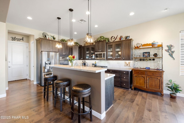 kitchen featuring appliances with stainless steel finishes, pendant lighting, dark brown cabinets, and a kitchen island with sink