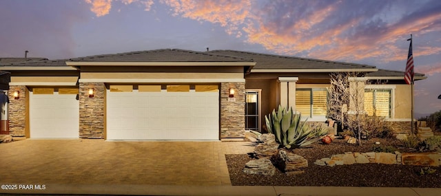 prairie-style home featuring a garage, stone siding, driveway, and stucco siding