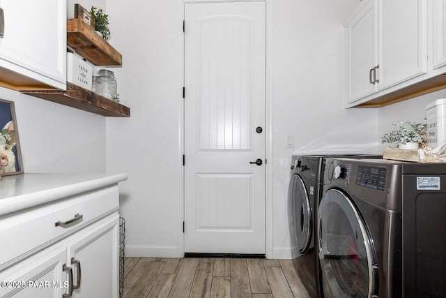 laundry area featuring cabinets, washing machine and clothes dryer, and light hardwood / wood-style flooring