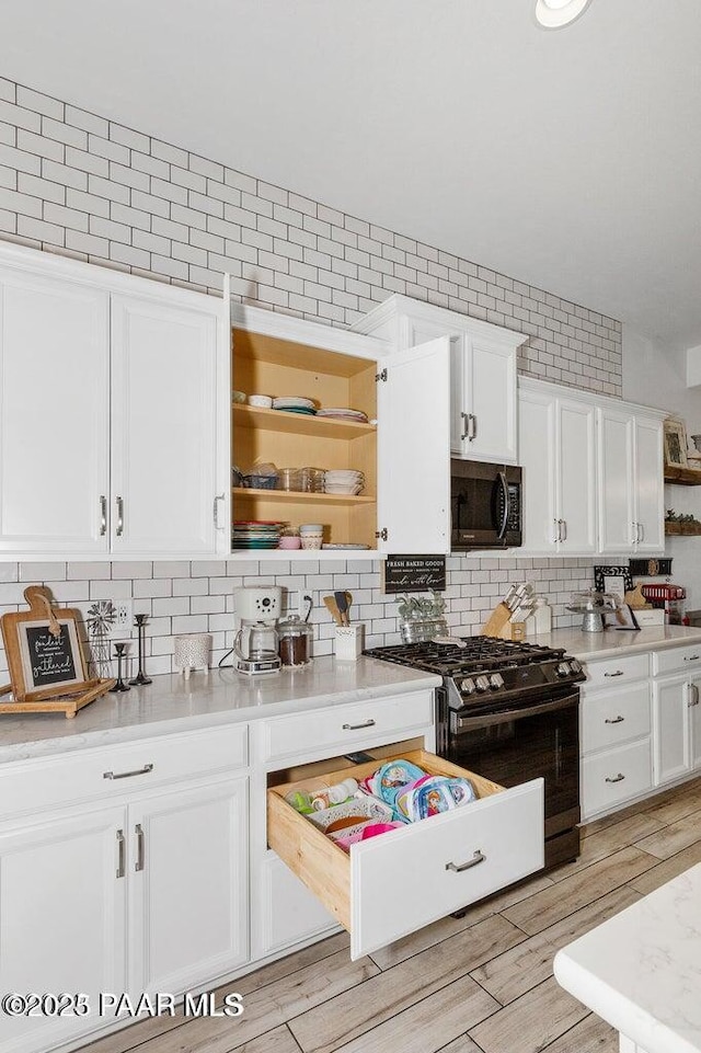 kitchen with white cabinetry, backsplash, light wood-type flooring, and stainless steel gas stove