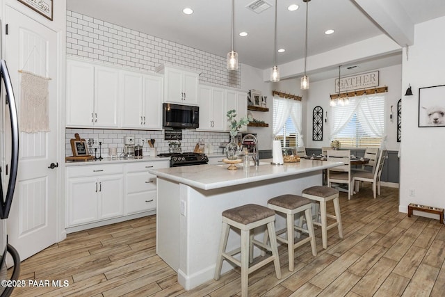 kitchen with black gas range oven, light hardwood / wood-style flooring, hanging light fixtures, an island with sink, and white cabinets