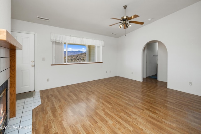 15015 E White Dr, Dewey-Humboldt, AZ 86327 - unfurnished living room featuring ceiling fan, light wood-style flooring, arched walkways, a tile fireplace, and lofted ceiling