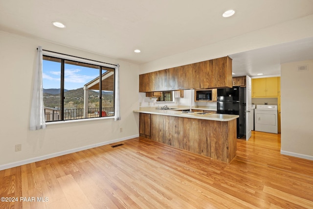 kitchen featuring kitchen peninsula, light wood-type flooring, washer and clothes dryer, black appliances, and a mountain view