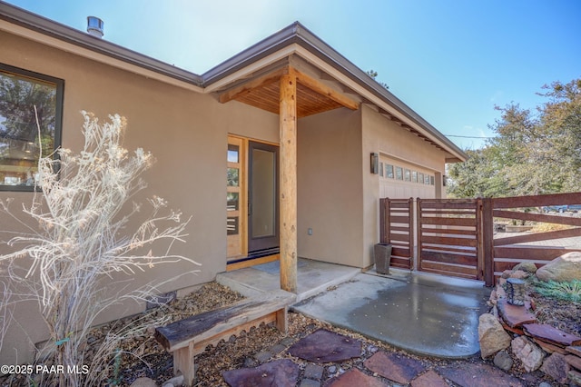 entrance to property with fence, an attached garage, and stucco siding