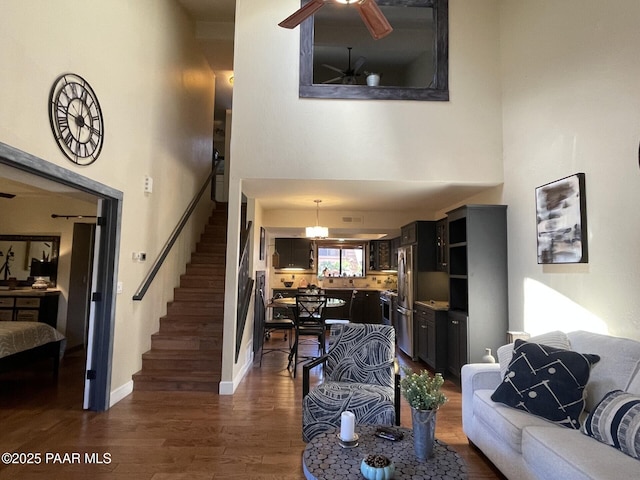 living area with dark wood-style floors, a ceiling fan, stairway, and a towering ceiling