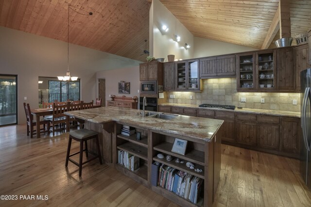 kitchen with light wood-style flooring, stainless steel appliances, decorative backsplash, and high vaulted ceiling
