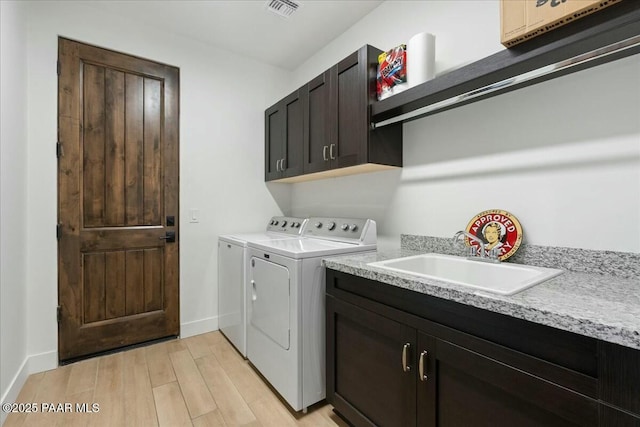 laundry area featuring cabinets, washing machine and dryer, sink, and light hardwood / wood-style floors