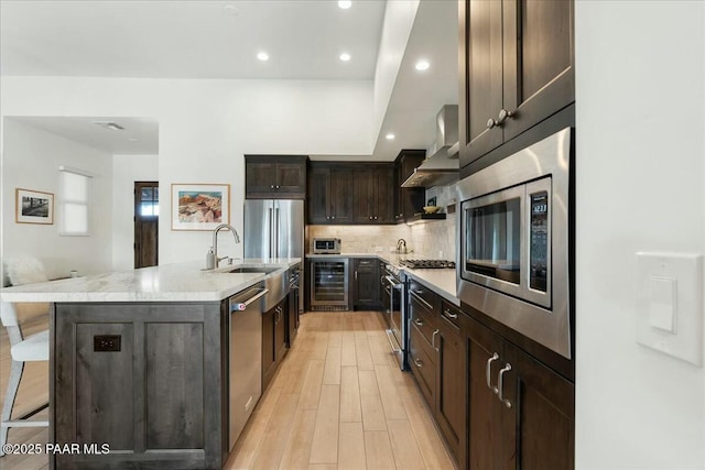 kitchen with an island with sink, a breakfast bar area, beverage cooler, stainless steel appliances, and wall chimney exhaust hood