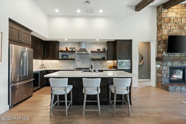 kitchen featuring wall chimney exhaust hood, sink, a breakfast bar area, stainless steel appliances, and a kitchen island with sink