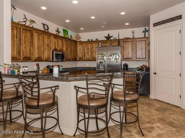 kitchen featuring a kitchen breakfast bar, kitchen peninsula, dark stone countertops, and stainless steel appliances