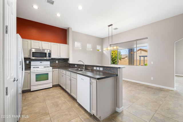 kitchen with a peninsula, white appliances, a sink, visible vents, and tasteful backsplash