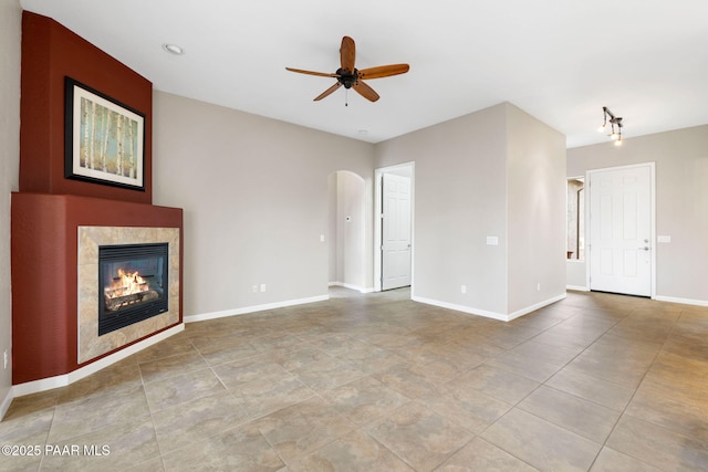 unfurnished living room featuring arched walkways, a fireplace, a ceiling fan, and baseboards