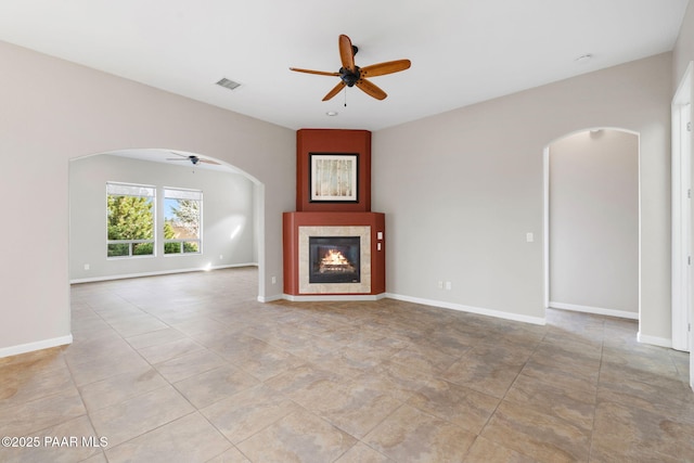 unfurnished living room with ceiling fan, visible vents, arched walkways, and a tile fireplace