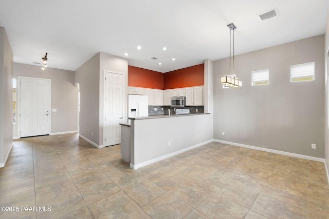 kitchen with a peninsula, white cabinetry, white fridge with ice dispenser, tasteful backsplash, and stainless steel microwave