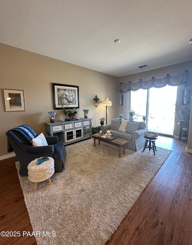 living room with visible vents, a textured ceiling, baseboards, and wood finished floors