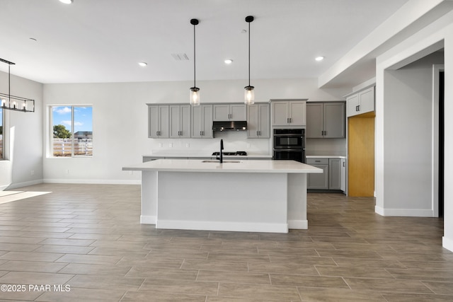 kitchen featuring an island with sink, sink, gray cabinetry, and pendant lighting