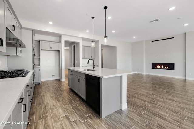 kitchen featuring sink, a kitchen island with sink, gray cabinetry, extractor fan, and black appliances