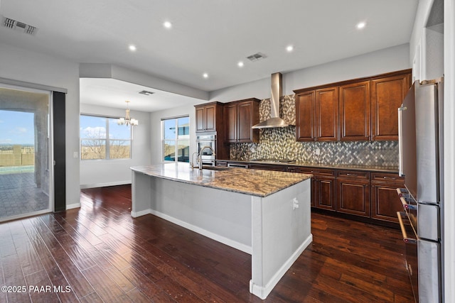 kitchen with visible vents, wall chimney exhaust hood, a kitchen island with sink, stainless steel appliances, and backsplash