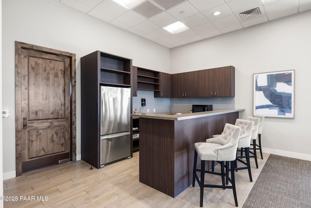 kitchen with a breakfast bar, open shelves, visible vents, backsplash, and freestanding refrigerator