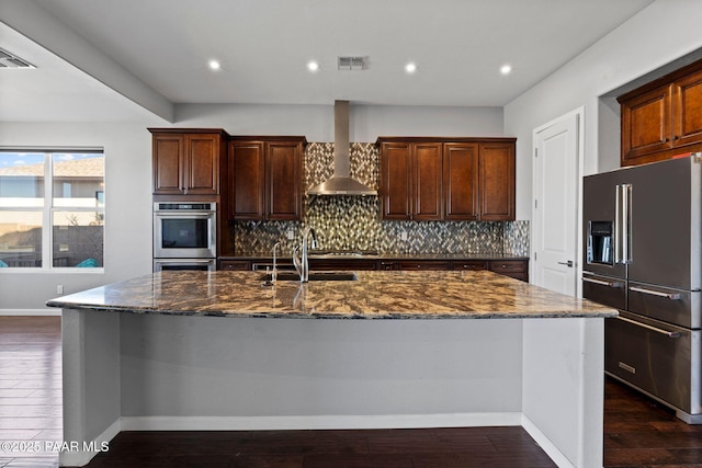 kitchen featuring dark wood-style flooring, high end fridge, decorative backsplash, a sink, and wall chimney range hood