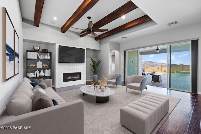 living area featuring a fireplace, wood finished floors, visible vents, a ceiling fan, and beamed ceiling