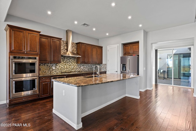 kitchen with visible vents, an island with sink, wall chimney exhaust hood, appliances with stainless steel finishes, and a sink