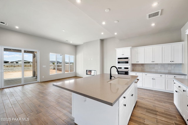 kitchen with visible vents, a center island with sink, and white cabinets