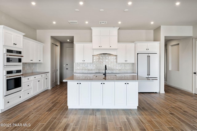 kitchen with white appliances, a sink, visible vents, white cabinetry, and an island with sink