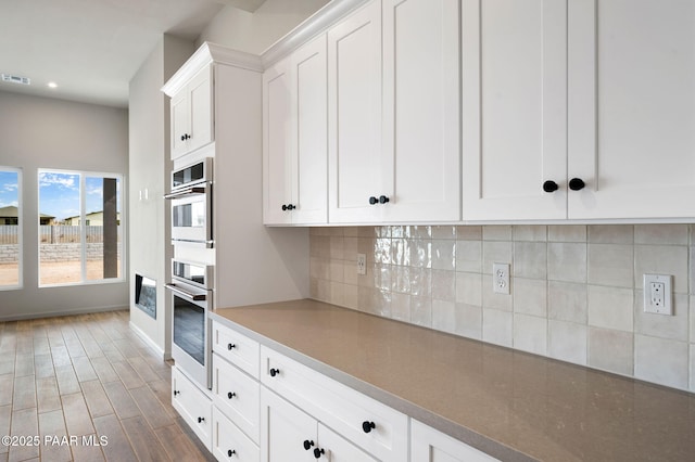 kitchen with dark wood-style flooring, tasteful backsplash, double oven, white cabinetry, and baseboards