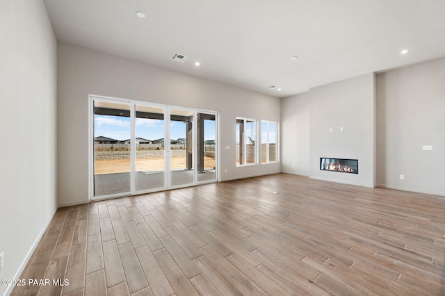 unfurnished living room with light wood-style flooring, recessed lighting, visible vents, baseboards, and a glass covered fireplace