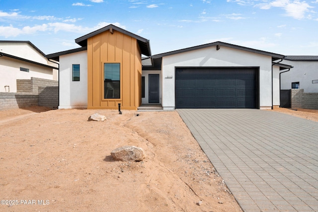 view of front of house featuring decorative driveway, stucco siding, board and batten siding, fence, and a garage