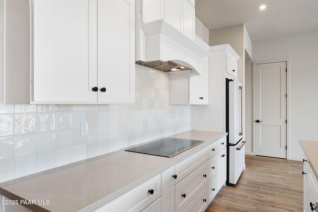 kitchen featuring custom exhaust hood, tasteful backsplash, light countertops, white cabinetry, and black electric cooktop