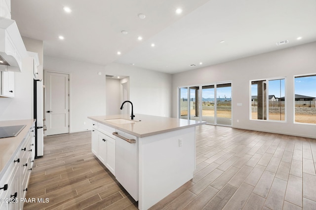 kitchen with white appliances, a sink, white cabinets, light countertops, and a center island with sink