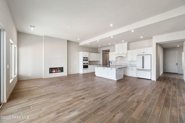 kitchen featuring open floor plan, a kitchen island with sink, visible vents, and white built in refrigerator