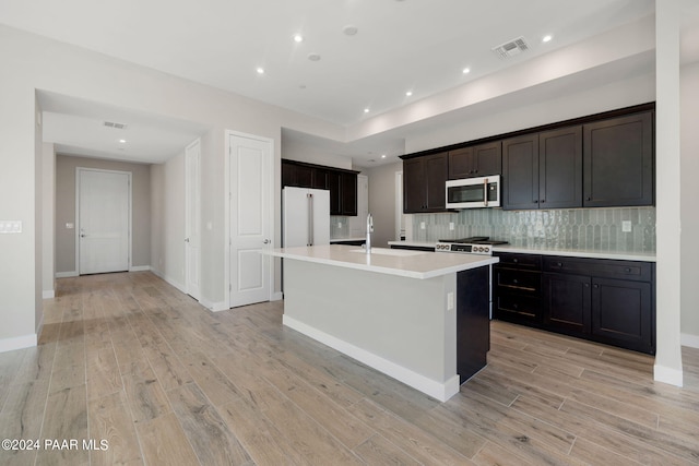 kitchen featuring sink, backsplash, light hardwood / wood-style floors, high end white refrigerator, and a center island with sink