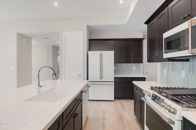 kitchen featuring sink, stainless steel appliances, tasteful backsplash, light stone counters, and light hardwood / wood-style flooring