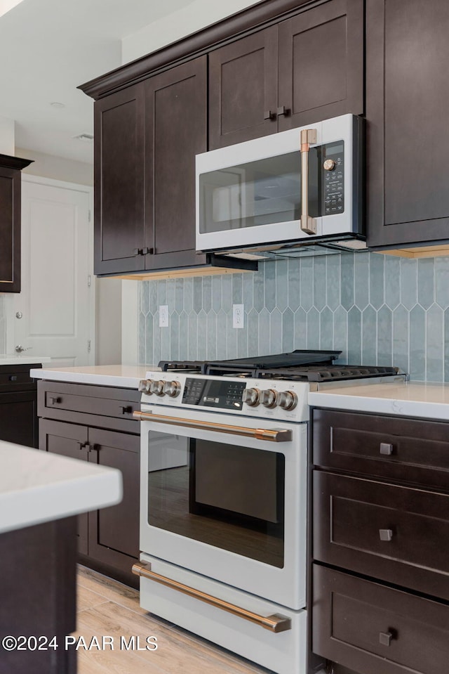 kitchen with dark brown cabinets, high end range, backsplash, and light hardwood / wood-style flooring