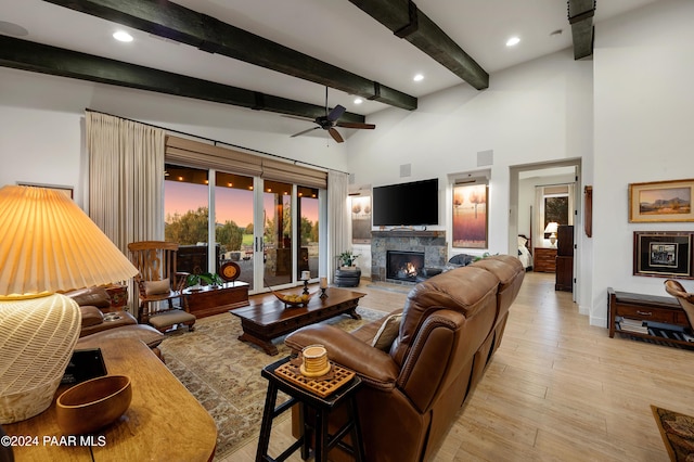 living room featuring beamed ceiling, ceiling fan, light wood-type flooring, and a towering ceiling